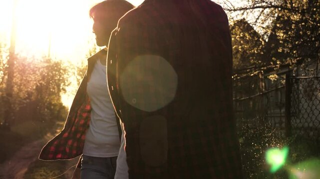 Two women are standing in a forest, holding hands and smiling at each other. The sun is shining brightly, casting a warm glow on the trees and the ground. The atmosphere is calm and tranquil