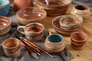 Different beautiful pottery and set of clay crafting tools on wooden table, closeup