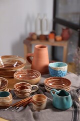 Different beautiful pottery and set of clay crafting tools on table indoors