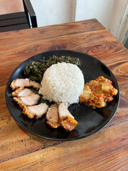 Indonesian chinese pork belly, Savoring a generous serving of fluffy rice accompanied by crispy pork belly , sautéed greens, and a side of flavorful sauce in a casual setting