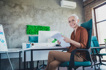 Photo of professional mature lady corporate leader sit table documents resumes wear brown shirt...