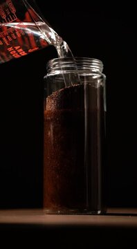 cold brew coffee pouring coffee grinds into water in a glass jar adding more water on black background vertical shot 