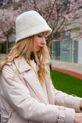 Stylish woman in a white fluffy bucket hat adjusting her coat outdoors