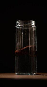 cold brew coffee pouring coffee grinds into water in a glass jar adding more water on black background vertical shot 