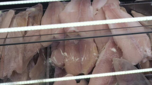 close up of frozen pollock fillets lying in a freezer behind glass.