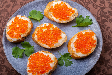 Canapes with red caviar on a plate decorated with cilantro
