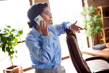 Young businesswoman in elegant blouse having a phone call in modern office interior with natural...