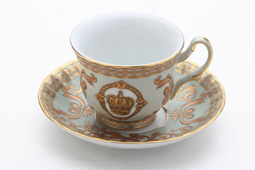 Golden-rimmed porcelain teacup bearing royal crown motif, symbolizing luxurious teatime elegance...
