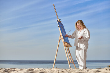 Young female artist painting on tranquil beach setting