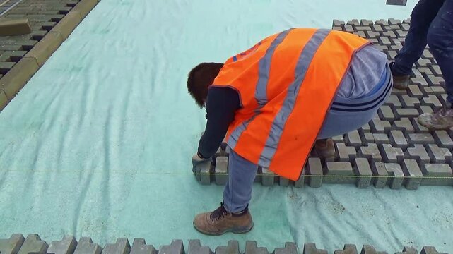 Construction site with workers laying interlocking concrete pavers. Close-up on the installation process, highlighting the precision and teamwork