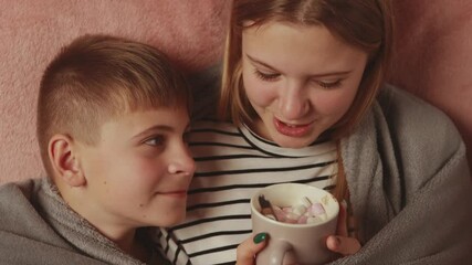 Sibling siblings huddling closely, sipping marshmallow-topped hot chocolate, snuggling under soft blanket during intimate winter bonding moment - Powered by Adobe