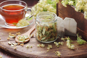 Linden dry herb in a glass jar with tea bags, cup of herbal drink and flowers in a wooden box on wooden rustic background, closeup, sleep and relax drink, natural medicine and naturopathy concept
