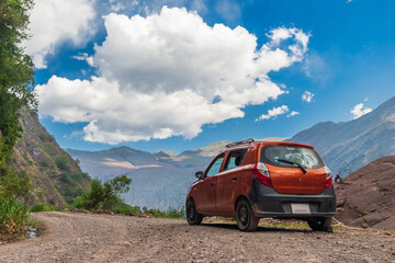 Un automóvil naranja con rastros de tierra se encuentra estacionado en un camino rural rodeado de...
