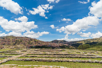  Ruinas de un sitio arqueológico en terrazas con una ciudad en las montañas de fondo. El cielo...