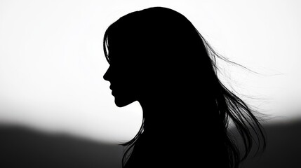 A woman stands in profile, her silhouette defined against a soft, illuminated backdrop as her hair gently sways in the breeze during sunset