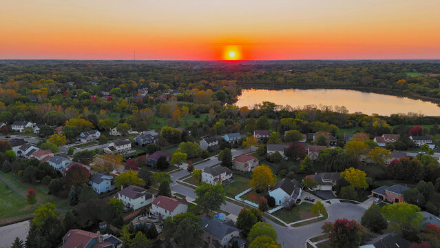 Sunset over Chicago suburban landscape. A captivating aerial view of a Chicago suburb at sunset with a vibrant orange sun sinking into the horizon.