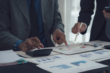 Financial Strategy Session: Two business professionals collaborate closely, reviewing financial data and charts, using a calculator and pen to analyze key performance indicators.  