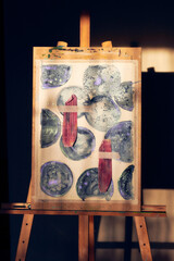 Abstract watercolor painting on a wooden easel, featuring circular and organic shapes in deep tones