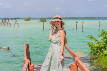 Female tourist in a turquoise dress standing on a wooden pier over the turquoise waters of Bacalar...