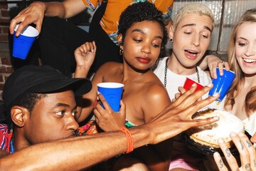 Group of friends at a party, holding drinks, reaching for a pie. Diverse group, laughing,...