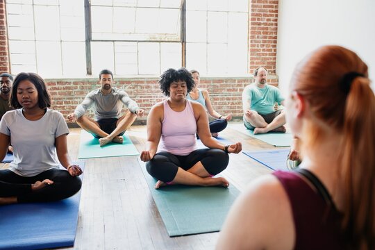 Diverse group of men and women practicing yoga. The yoga class includes various ethnicities, with participants sitting on yoga mats. Yoga for relaxation and fitness. Exercise and yoga for well being.