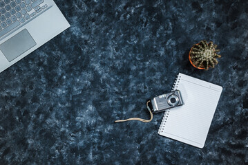 Laptop, pocket camera and notebook on abstract black table