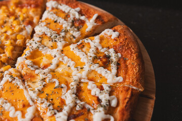 Detail view of a piece of pizza with different types of cheese on a round wooden board.