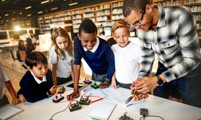 Diverse group of students in a library, learning electronics with teacher. Students and teacher engage learning electrical circuit. Teacher teach students electrical circuit. Technological education.