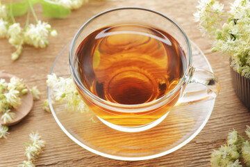 Linden herbal tea in a glass cup with flowers on wooden rustic background, closeup, sleep and relax drink, natural medicine and naturopathy concept