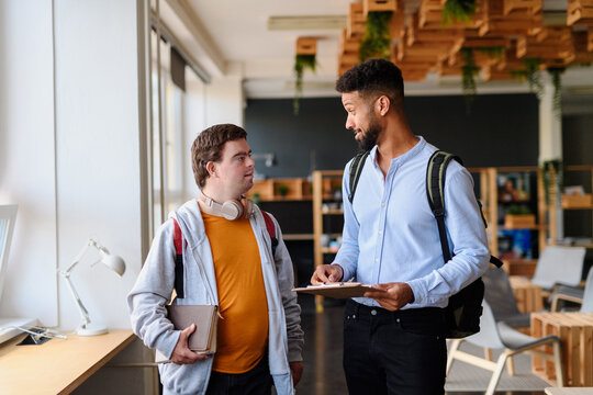 Young man with Down syndrome and his teacher talking while walking down the school hallway.
