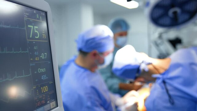 Some numbers on the monitor of lung ventilator working at operation. Team of male surgeons works at backdrop in blur.