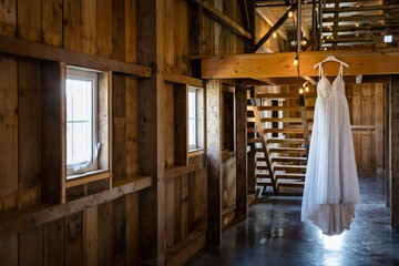 Elegant white wedding dress hanging in a rustic barn