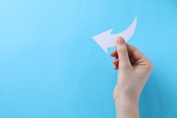 Woman with paper arrow on light blue background, top view. Space for text