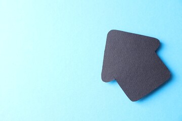 One black paper arrow on light blue background, top view. Space for text