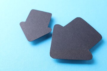 Two black paper arrows on light blue background, closeup