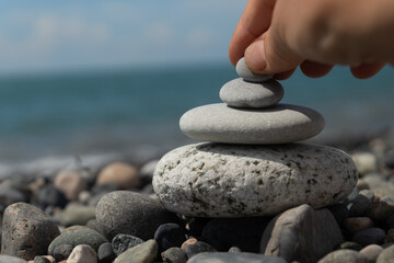 A human hand builds a pyramid of pebbles on the seashore, embodying the concept of Zen, meditation and relaxation