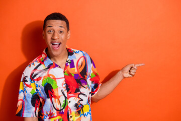 Joyful young man with vibrant, colorful shirt enthusiastically pointing against an orange...