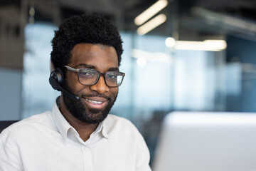 Obraz premium Portrait of a support worker, a man with a headset smiling and looking at the camera. A company employee close-up with a laptop inside the office