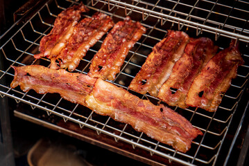 Crispy Bacon Strips Being Slow-Cooked in a Smoker at a Backyard Barbecue During a Sunny Afternoon Gathering With Friends and Family.