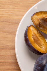 Close-up of halved plums on a white plate with wooden background

