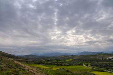 Rolling green hills stretch under a cloudy sky with distant mountains in the background