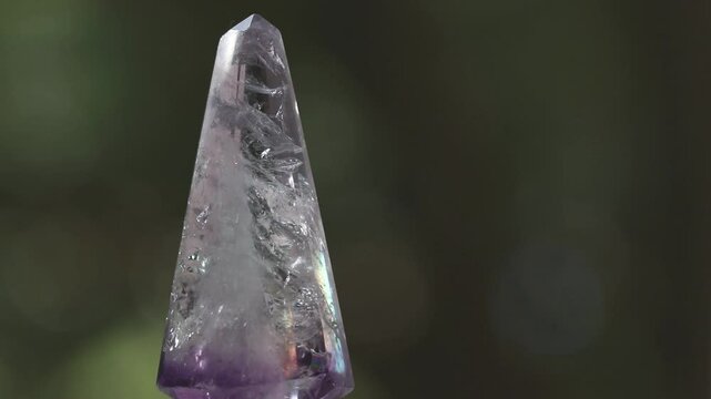 Rotating faceted amethyst crystal and dark background.