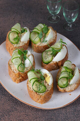 Bruschetta with tuna pate, egg and cucumber on white plate on brown background