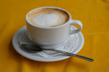 Warm cappuccino in a white cup sits elegantly on a vibrant yellow tablecloth