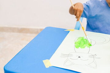 Latin american boy painting a cat at home with green tempera