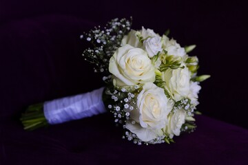Elegant bridal bouquet of white roses, lisianthus, and baby's breath, beautifully arranged against a dark background.