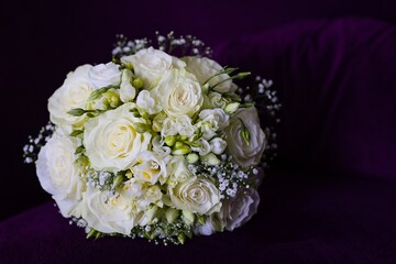 A delicate wedding bouquet with white roses, eustoma, and gypsophila, softly illuminated against a deep, moody backdrop.