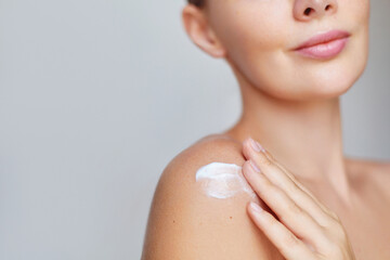 Bodycare. Beauty portrait of a woman applying moisturizing body care cream or lotion to her shoulder, emphasizing skincare and self-care on a soft, neutral background.