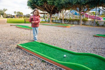 Fototapeta premium Little girl playing mini golf outdoor. Child having fun with new activity in spring time. Family vacations or resort.