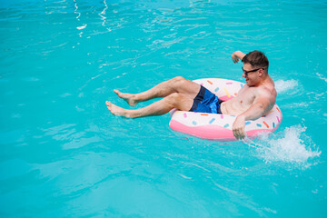 A cute man in shorts swims in the pool on an inflatable ring. Summer vacation in the pool of a single man.